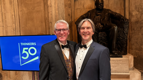 Two men in tuxedos standing in front of a sign that reads Thinkers50