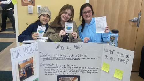 Three students from Dartmouth's Energy Justice Clinic at a table with a sign
