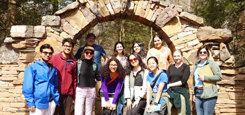 A group of Dartmouth students and staff pose for a photo below a stone archway.