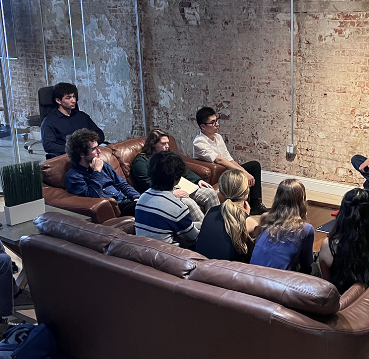 A group of people sitting on a couch and a chair in a start-up type office with brick walls and glass