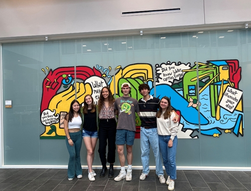 A group of students standing in front of a colorful mural