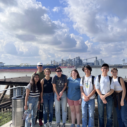 Student group posing in front of Mississippi River; many refineries in the background