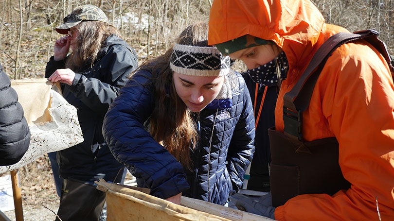 Two students standing in a river bed looking at a soil sample