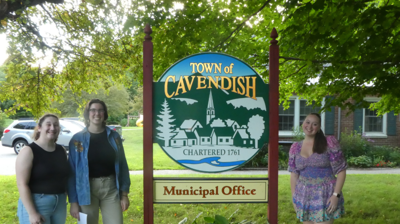 Three young women standing in front of a sign for the town of Cavendish, VT