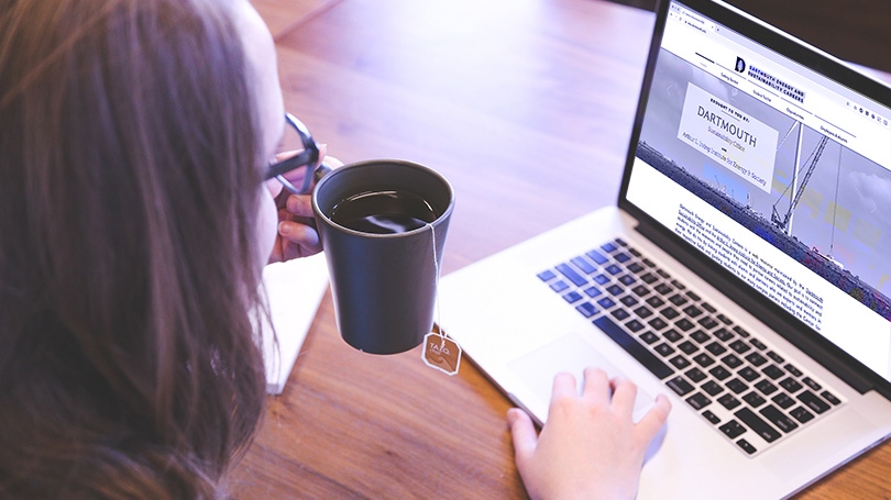 woman looking at laptop holding a cup of tea