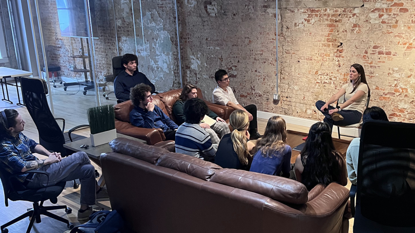A group of people sitting on a couch and a chair in a start-up type office with brick walls and glass