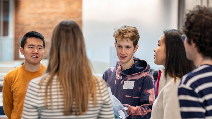 An image of five students standing in a semi-circle talking