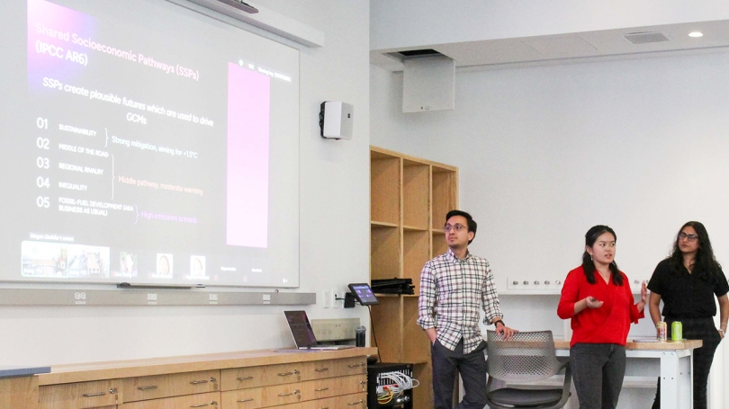Three people stand in front of a projector screen with an image titled 'Shared Socioeconomic Pathways.'