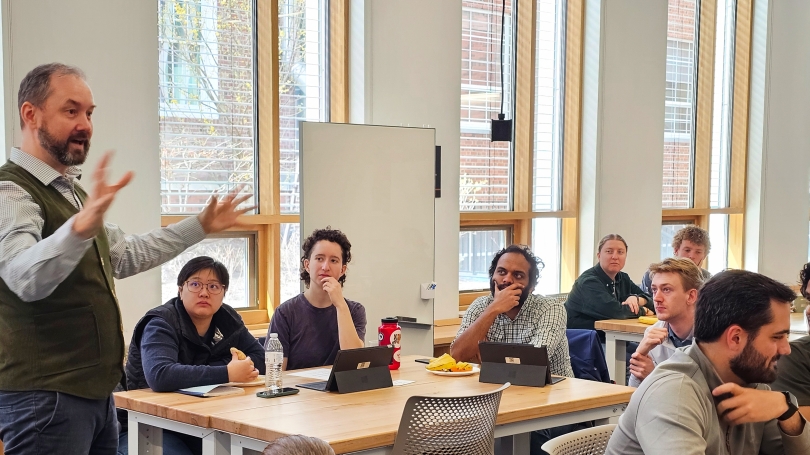 An instructor stands and speaks to a class of seated students.