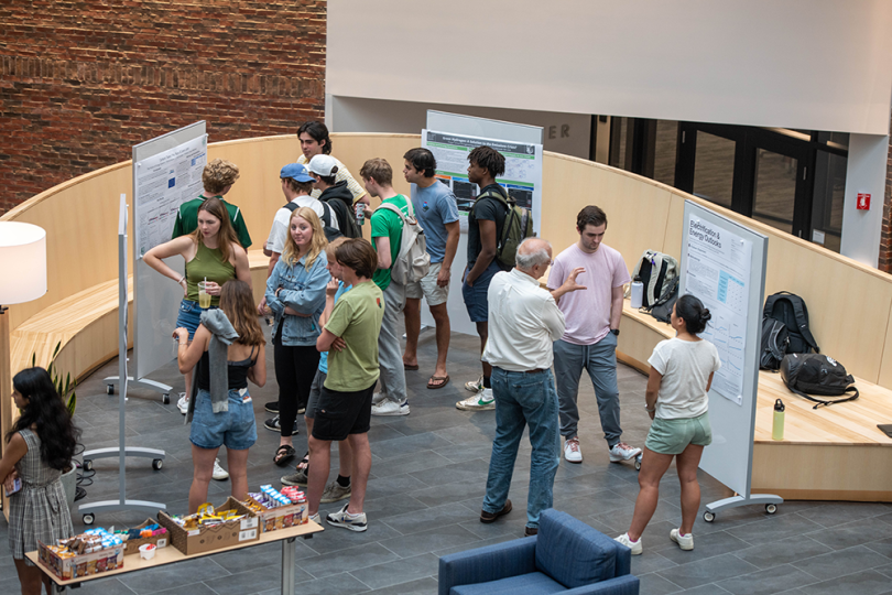 A view from above of a poster session in the Atrium with students and faculty standing around in a group looking at posters
