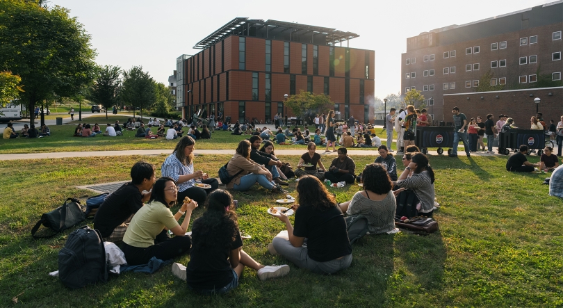 Groups of graduate students sit and eat on the grass in front of Anonymous Hall on the Dartmouth campus.