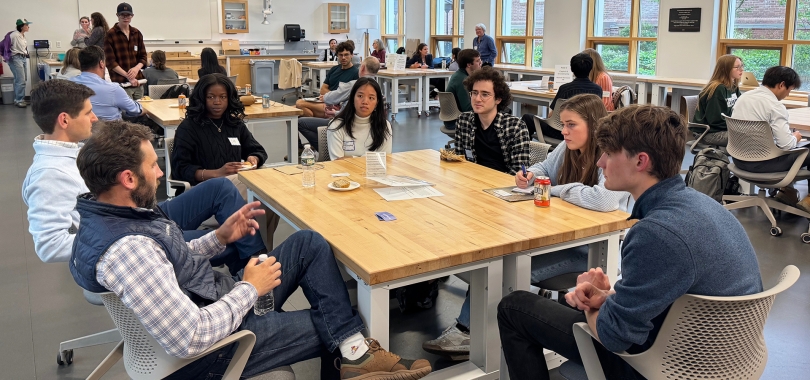 Mentors and students sit at tables in a large room and talk.