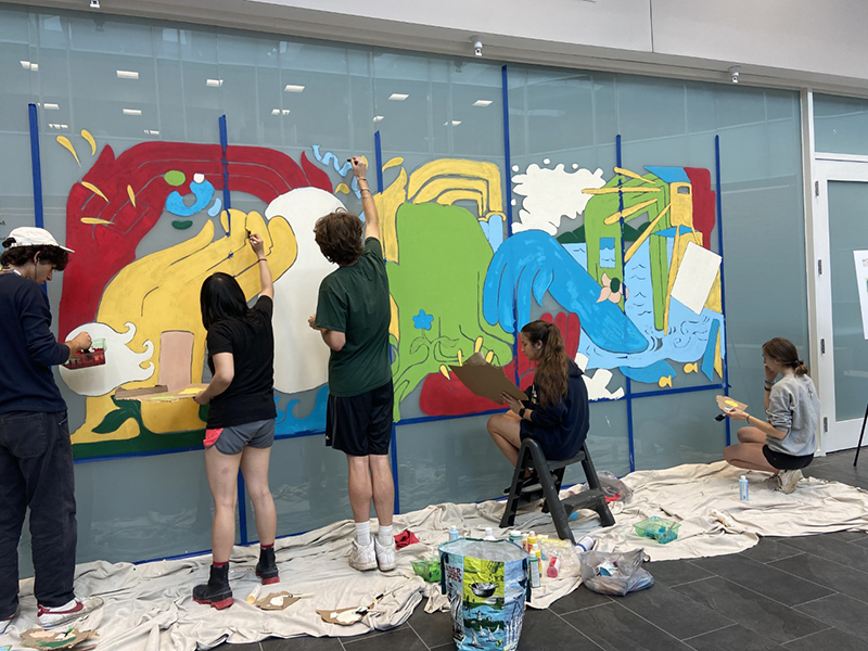 student artists working on painting a mural on a glass wall
