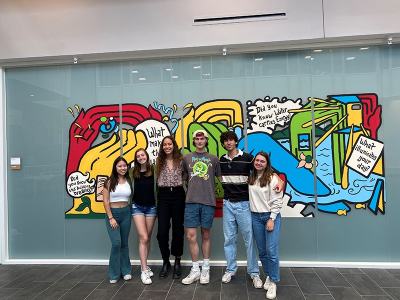 A group of students standing in front of a colorful mural