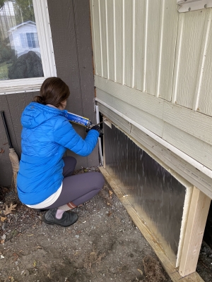 A person crouching next to the base of a mobile home with a foam insulation gun
