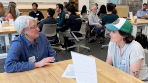Two people sit and talk with each other in a large room with many other seated, talking people.