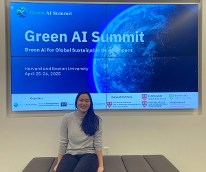A woman sits on a bench in front of a large screen with the words "Green AI Summit."