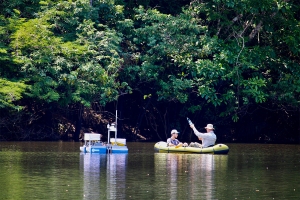 Two people sit in a yellow raft next to a robot, floating in a lake.
