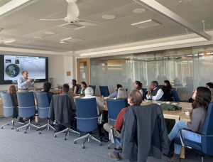 Faculty and research staff gather around a large table and listen to a presentation by Donald Perovich.