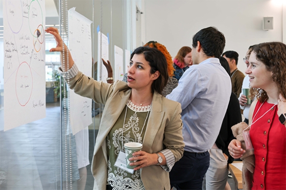 A woman points to a poster on a wall and talks with another woman standing behind her.